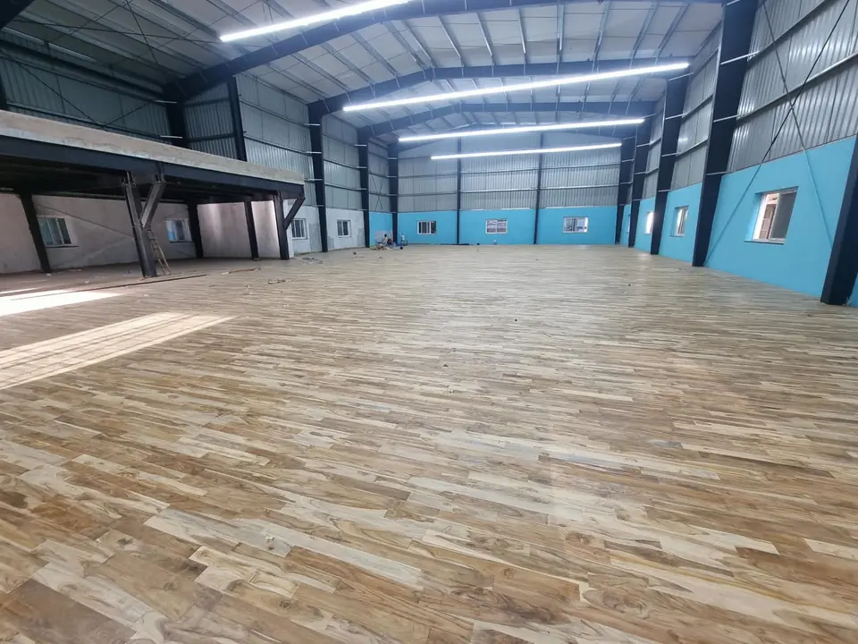 Wide view of a large teak wooden sports floor in a steel shed with a mezzanine and light blue lower walls.