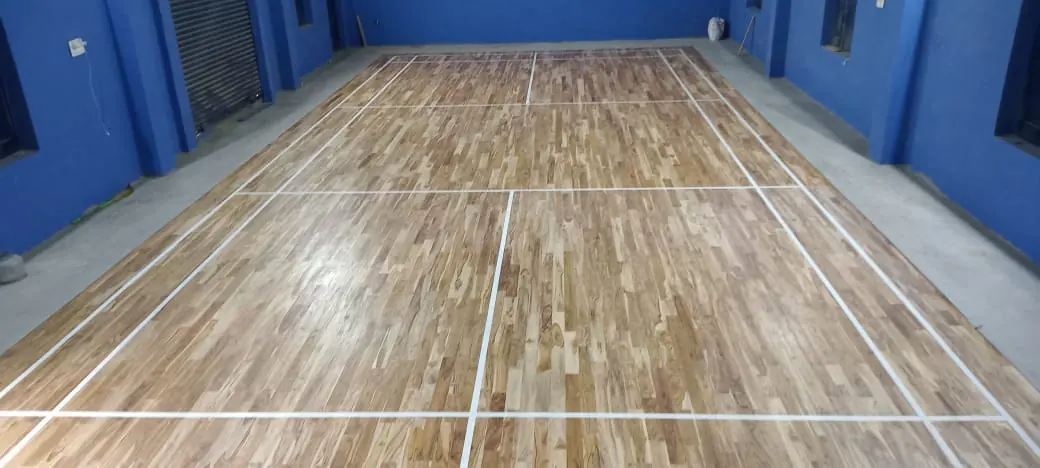 Teak Wooden Badminton Court Flooring with crisp white court lines in a blue-walled indoor hall.