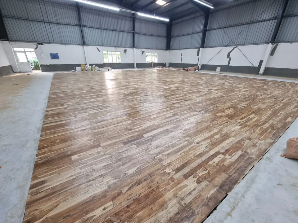 Freshly finished teak wooden sports floor with a soft sheen inside a steel-roofed shed with white walls.